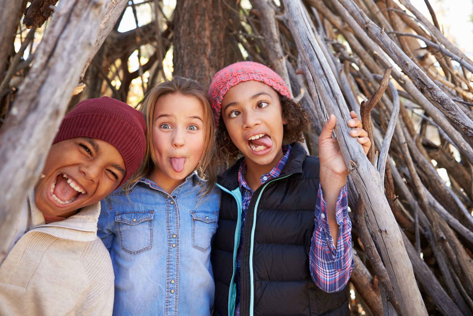 Three children pulling funny faces inside a den made of branches
