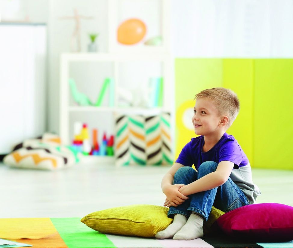 A young boy sitting on floor cushions in a bright, calm playroom